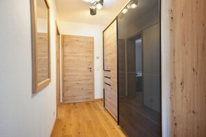 A hallway with wooden flooring, a mirrored wall, and a sliding door leading to a room. - Apartment "Einklang" with Mountain View, Balcony, and Wi-Fi (Krün)