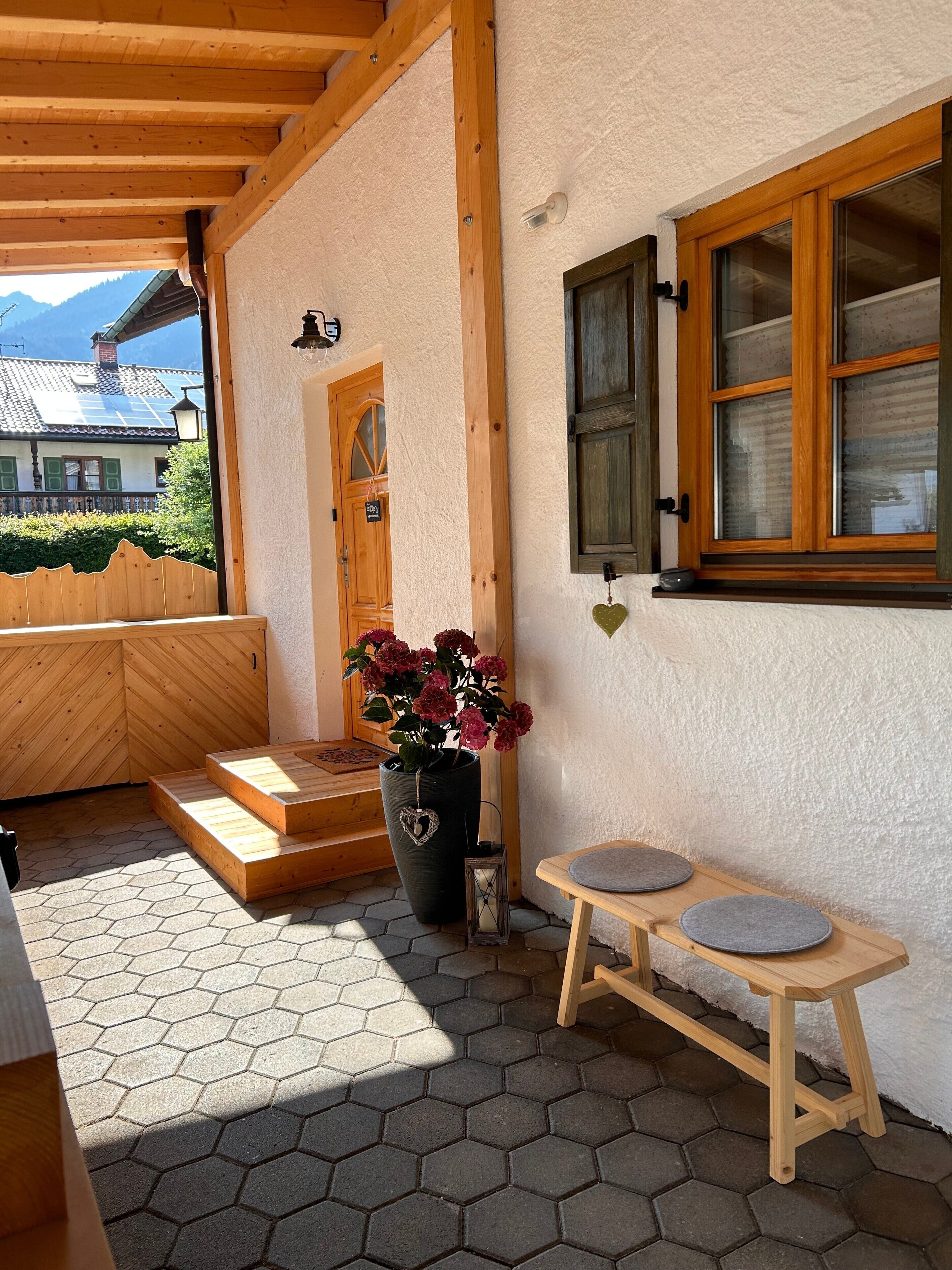 Une façade en bois avec une porte, un pot de fleurs et une petite table avec un coussin.