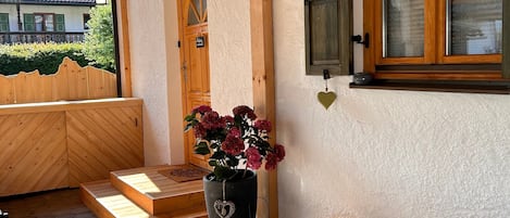 Une façade en bois avec une porte, un pot de fleurs et une petite table avec un coussin.