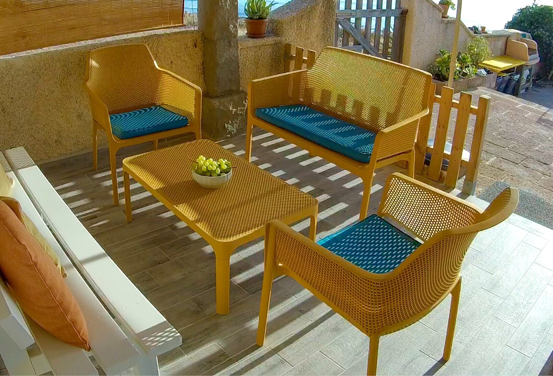 Un espace patio aménagé avec des meubles en osier, comprenant un canapé, deux fauteuils et une table, sur laquelle se trouve un saladier rempli de fruits.