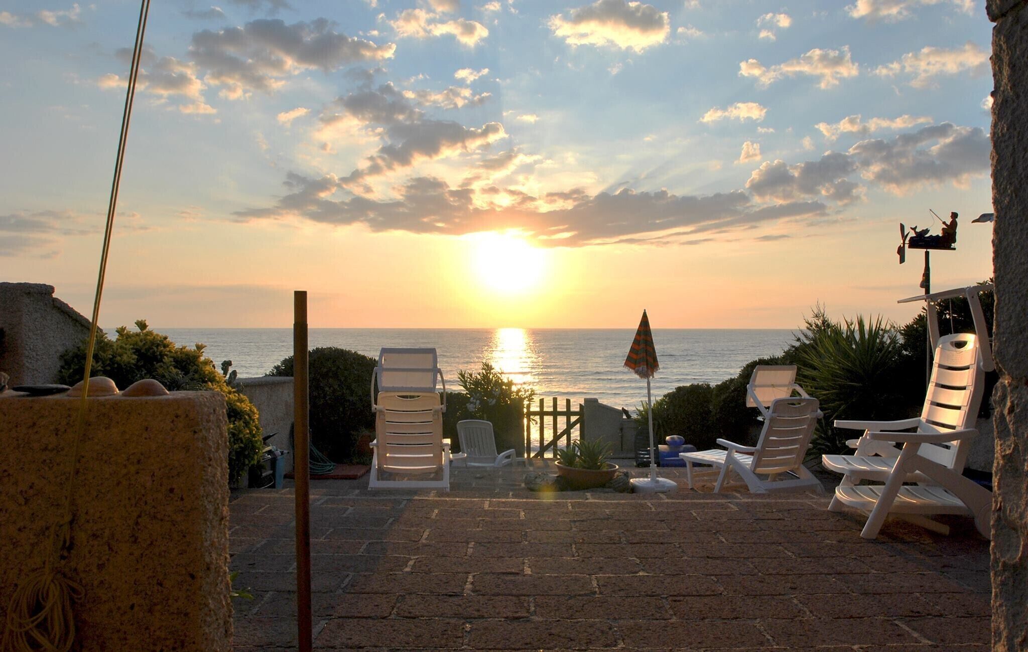 A patio with lounge chairs facing a sunset over the sea.