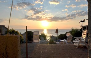 Eine Terrasse mit Liegestühlen, die auf einen Sonnenuntergang über dem Meer blickt.