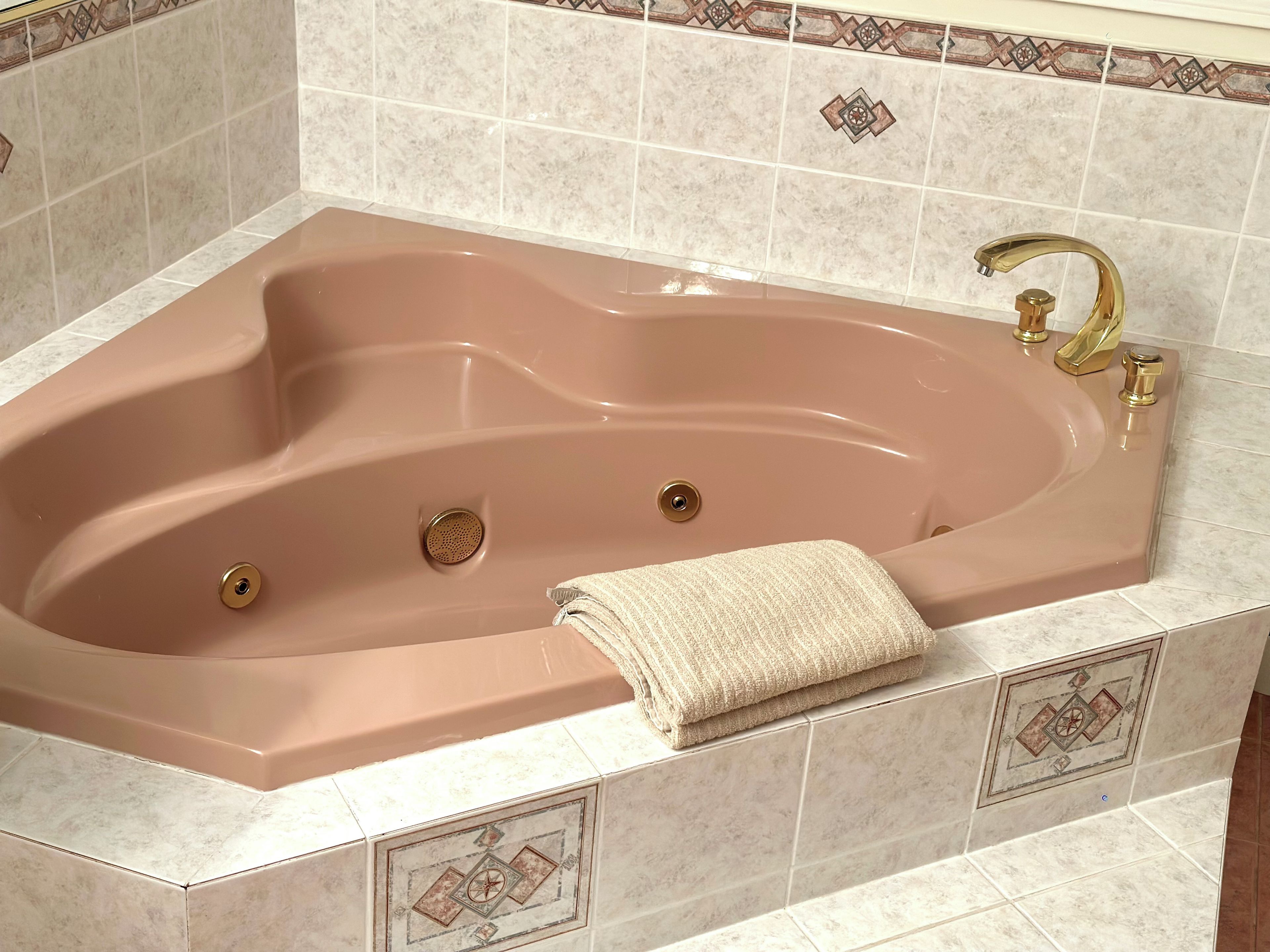 A rectangular bathtub with a single faucet and a drain, set in a tiled bathroom with decorative patterns.