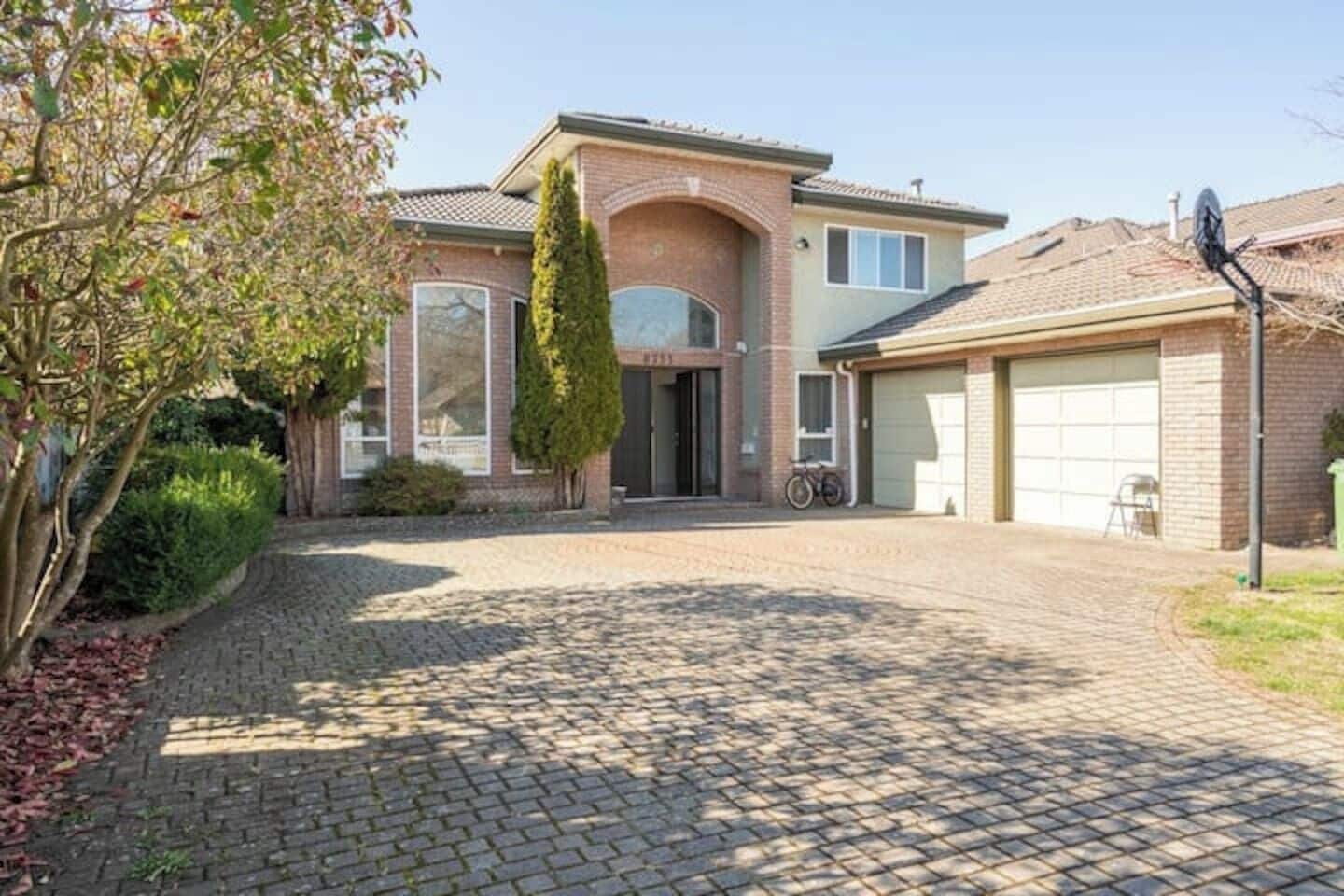 Une maison d’habitation avec une allée pavée, un garage et une antenne parabolique.