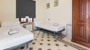 Una camera d'albergo con due letti, un comodino con una lampada, un tavolino con un cesto e un'armadio in legno.