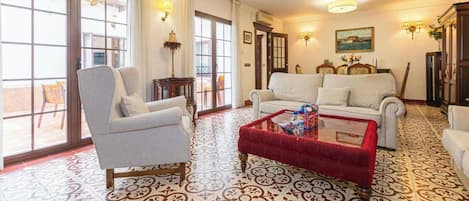A living room with a sofa, armchairs, a coffee table, and patterned floor tiles.