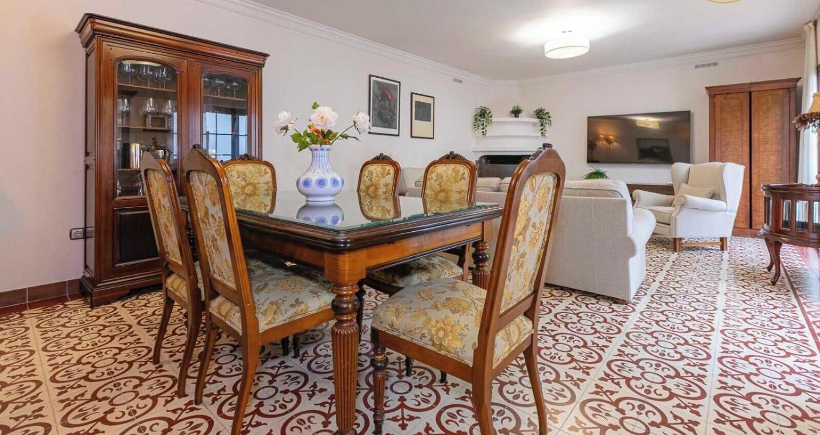 Un coin repas avec une table et des chaises en bois, un meuble avec des portes en verre et un sol à motifs.
