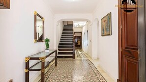 Un corridoio con una scala, un tavolino consolle con una pianta, pavimento a motivi e un quadro appeso al muro.