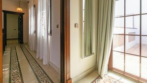 Un corridoio con pavimento decorato, una porta illuminata da un lampadario e una finestra con tende.