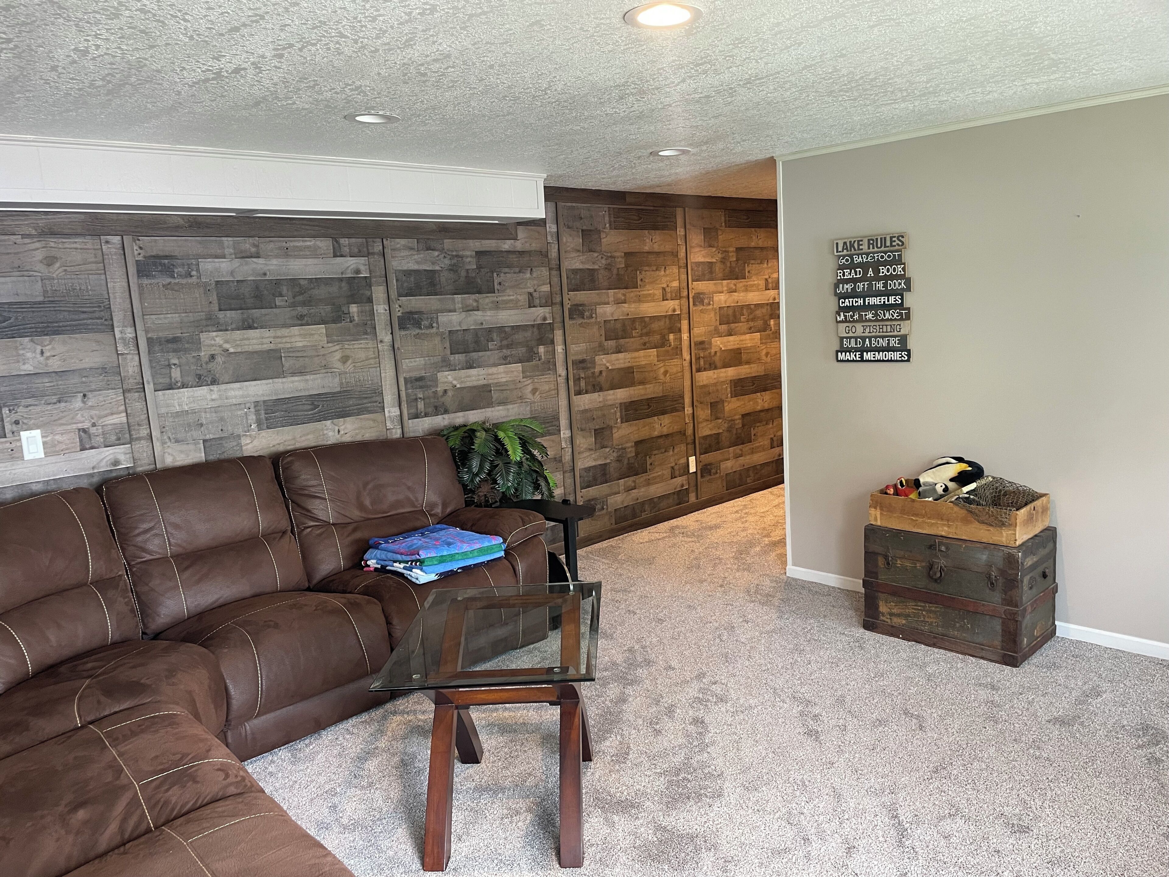 A living room with a brown leather sectional sofa, a glass coffee table, and a wooden wall panel.