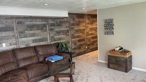 A living room with a brown leather sectional sofa, a glass coffee table, and a wooden wall panel. - Beautiful lakefront home on beautiful Crooked Lake (Angola)