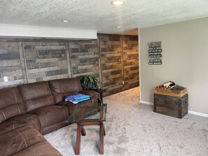 A living room with a brown leather sectional sofa, a glass coffee table, and a wooden wall panel. - Beautiful lakefront home on beautiful Crooked Lake (Angola)