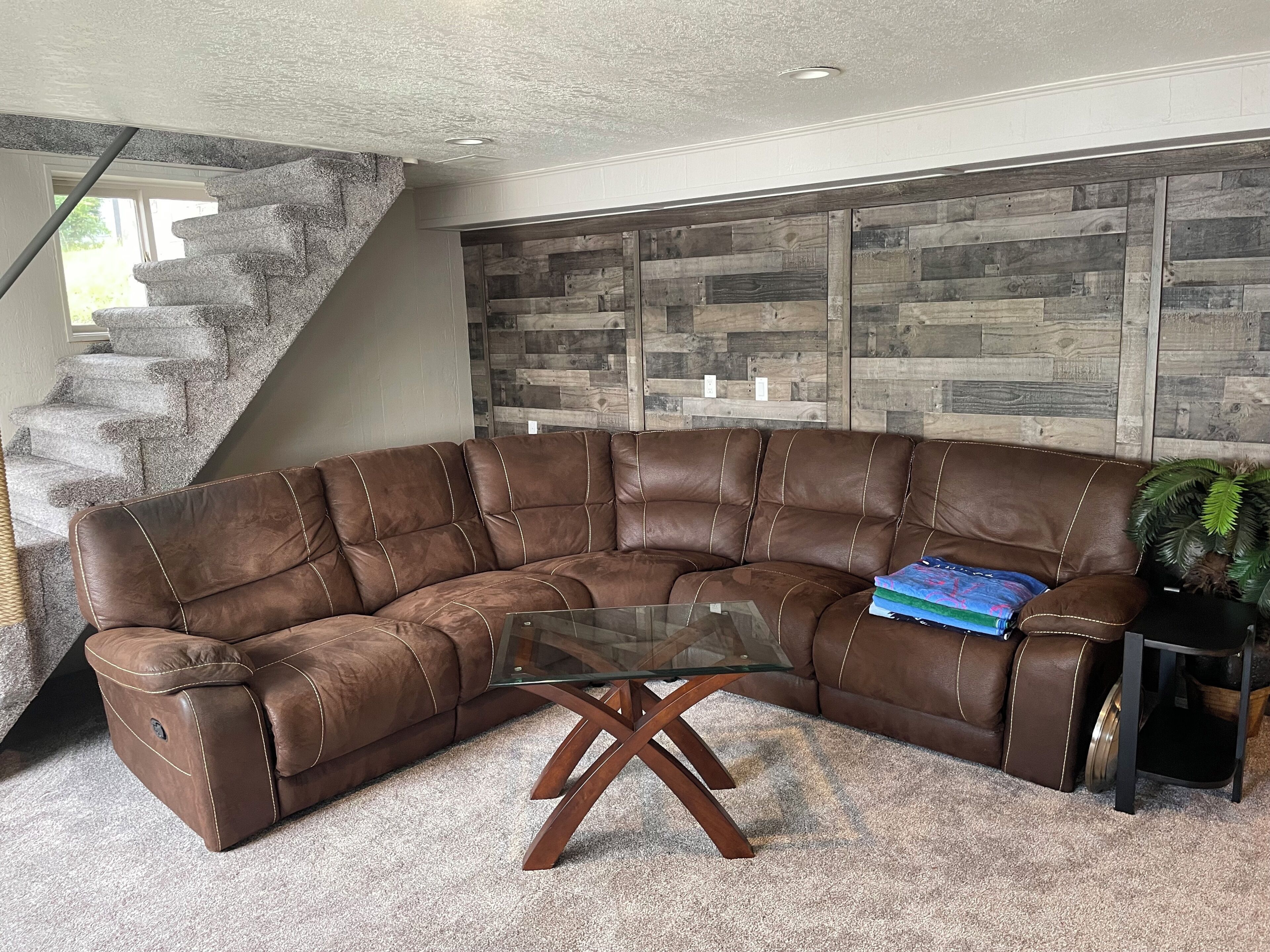 Ein braunes, ledernes Ecksofa mit einem Glastisch in einem Wohnzimmer mit einer Steintreppe und einer Holzwandverkleidung.