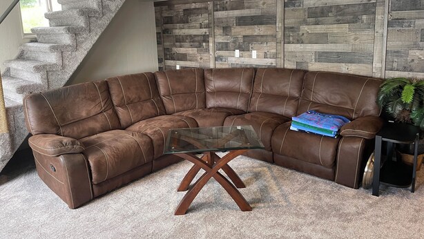 A brown leather sectional sofa with a glass coffee table in a living room with a stone staircase and a wooden wall panel. - Beautiful lakefront home on beautiful Crooked Lake (Angola)