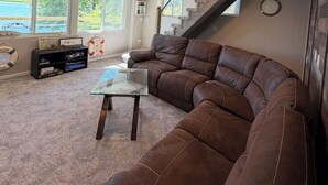 A spacious living room with a large brown leather sectional sofa, a glass coffee table, and a staircase leading to an upper level. - Beautiful lakefront home on beautiful Crooked Lake (Angola)