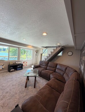 A spacious living room with a large brown leather sectional sofa, a glass coffee table, and a staircase leading to an upper level. - Beautiful lakefront home on beautiful Crooked Lake (Angola)