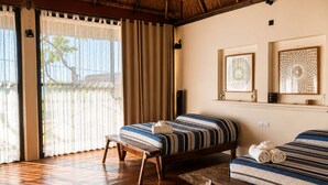 A room with two beds, a bench, a large window with curtains, and wall art. - Mytos By Grupo Chulel (Isla Aguada)