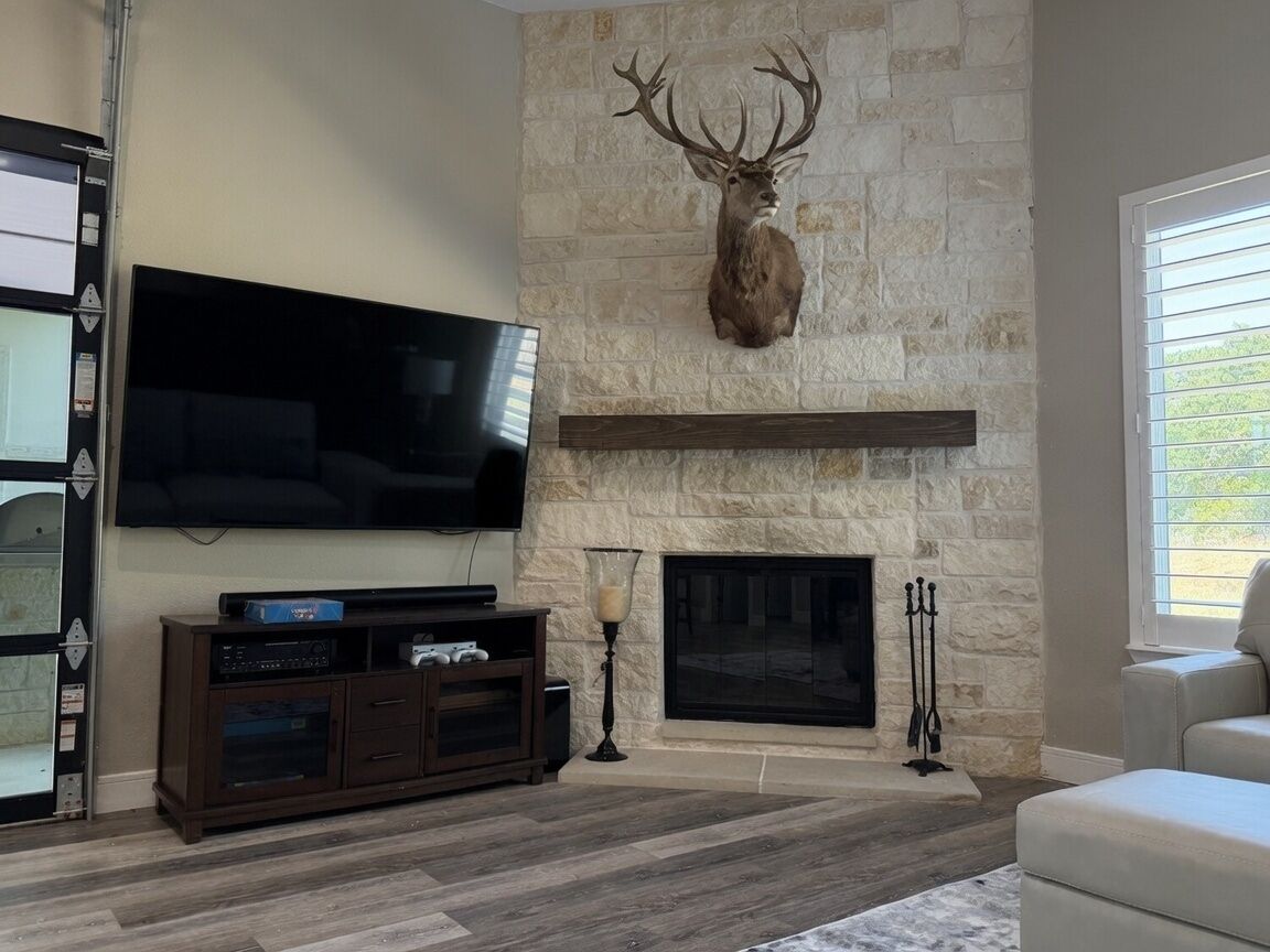 A living room with a stone fireplace, mounted television, and a large deer head.