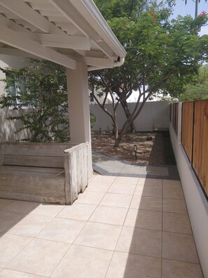 A covered patio area with a tiled floor, a wooden bench, and a tree. - Solara Suite I Sunny Studio I Private Plunge Pool (Noord)