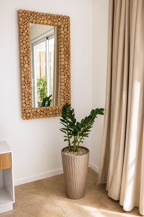 A room with a wooden bead wall mirror, a potted plant, a white console table, and beige curtains. - Solara Suite I Bright Studio I Private Diving Pool (Noord)