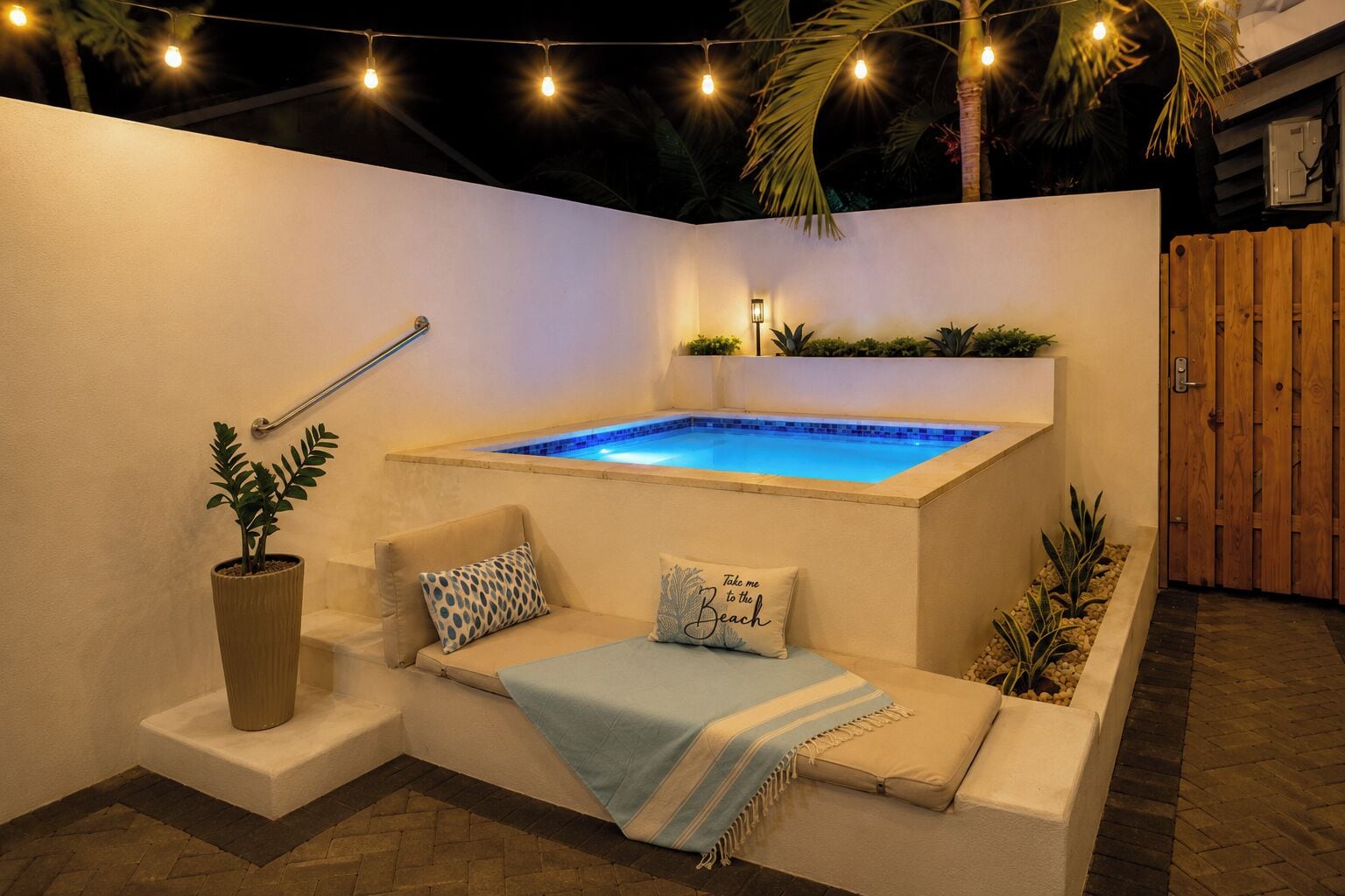 A spa area with a hot tub, a cushioned seating area, a potted plant, and a wooden fence.