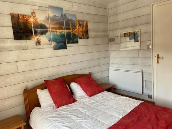 A bedroom with a wooden headboard, a bed with white and red bedding, and three landscape paintings on the wall.