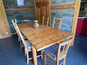 A wooden dining table with six chairs, a jar of candies, and a stone wall in the background.