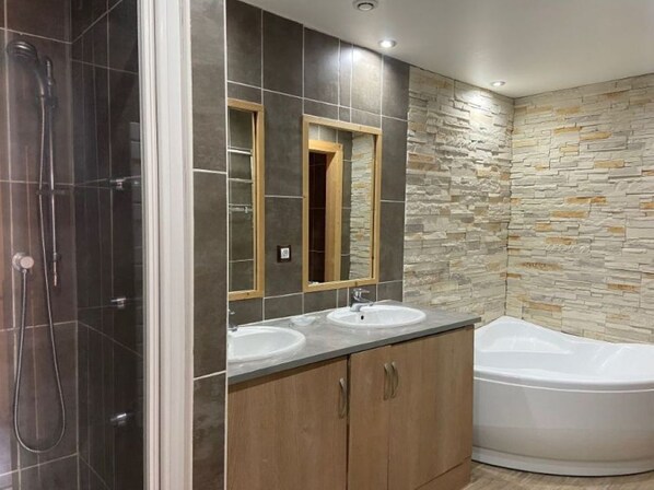 Ein Badezimmer mit Dusche, zwei Waschbecken, einem Spiegel und einer Badewanne.