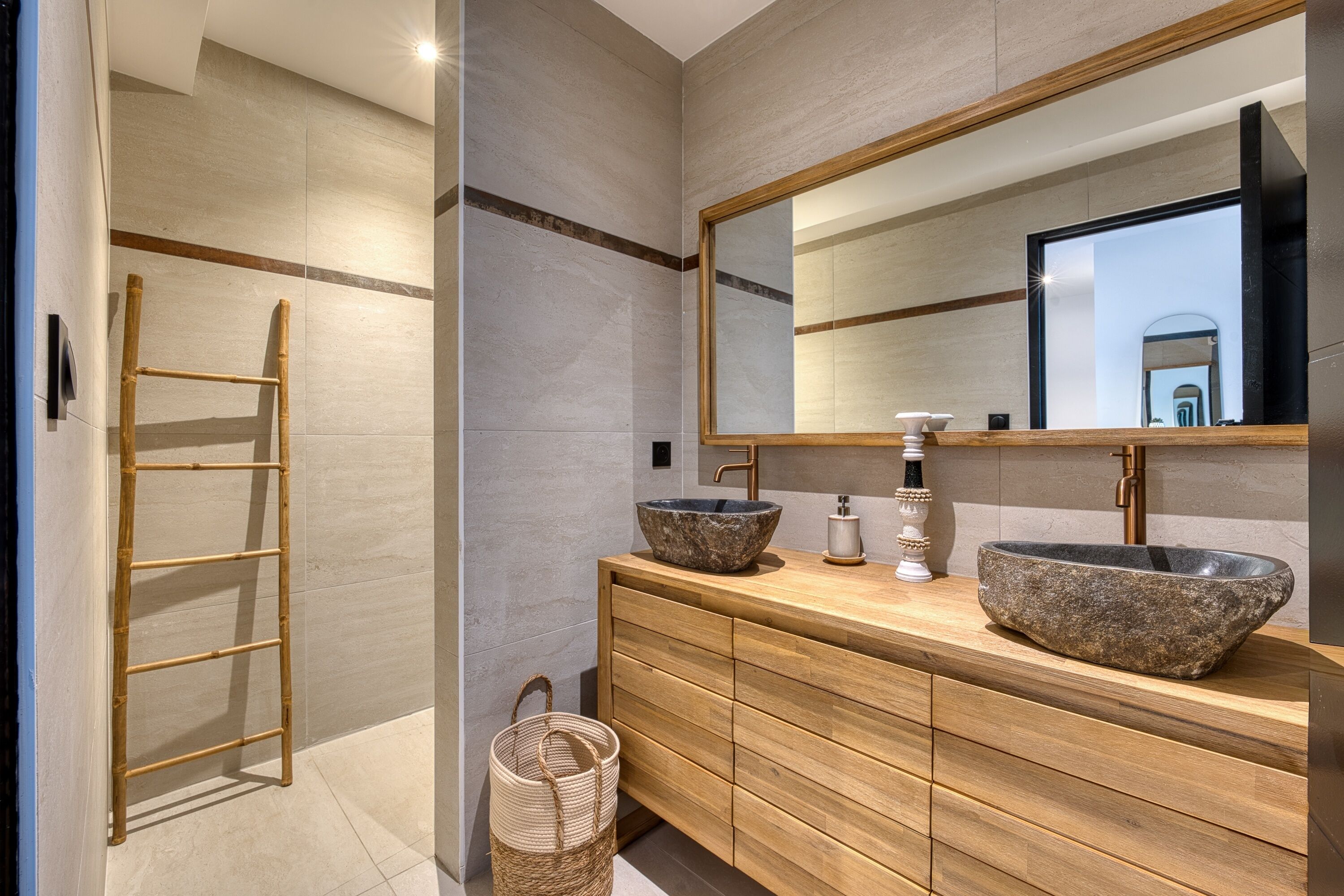 A modern bathroom with a wooden vanity, two stone sinks, a large mirror, and a glass shower enclosure.