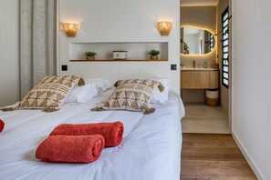 A hotel room with a bed, two wall-mounted sconces, a shelf with decorative items, a mirror, and a wooden floor. - Le Vakoa - Kaz Suspendue, entre lagons et sommets (Saint-Leu)