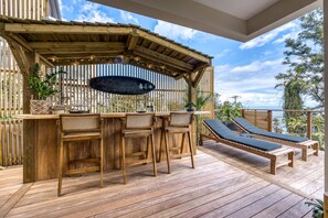 A wooden deck with a bar area, lounge chairs, and a pergola. - Le Vakoa - Kaz Suspendue, entre lagons et sommets (Saint-Leu)