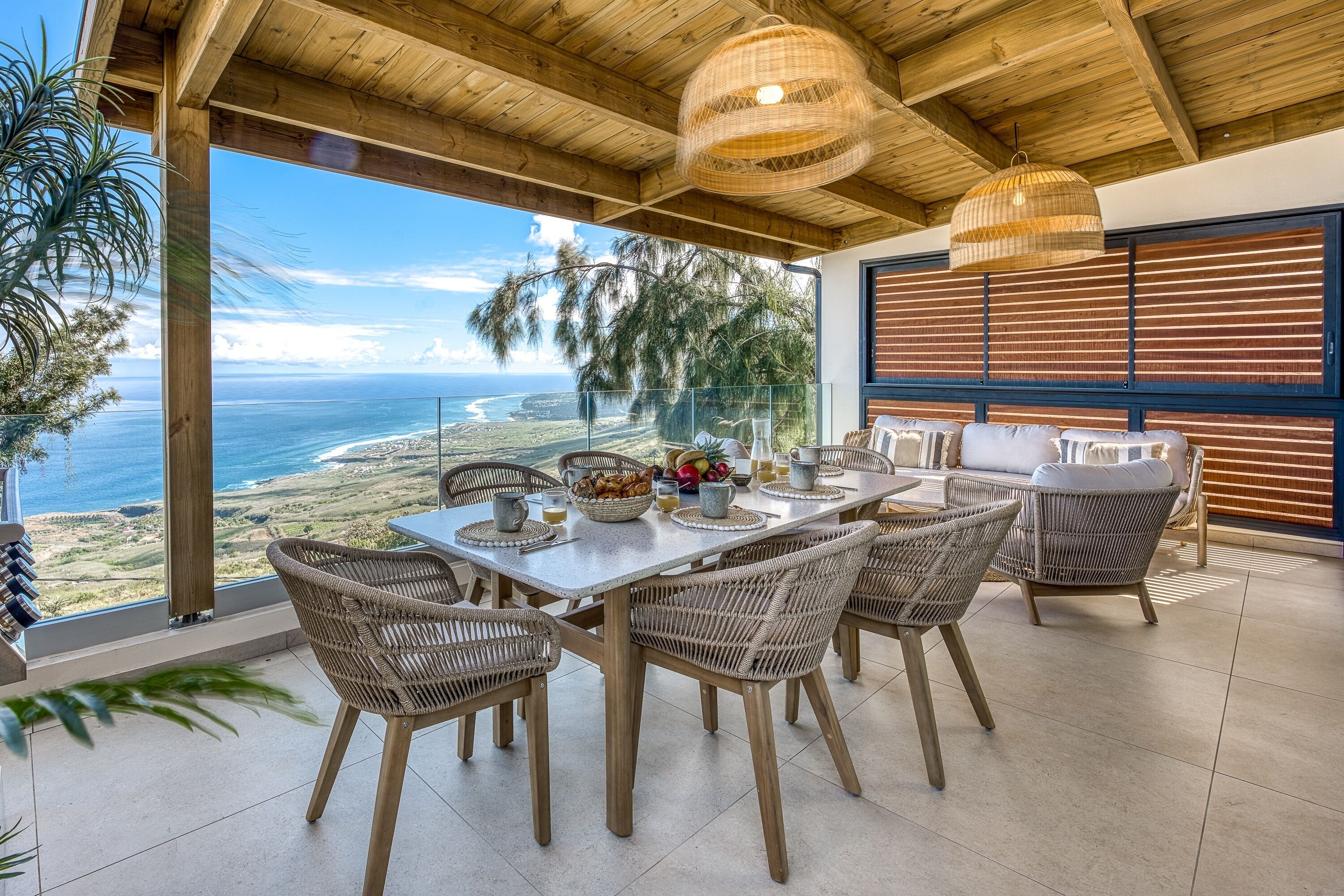 A dining area with a table and chairs, a view of the ocean, and a wooden ceiling.
