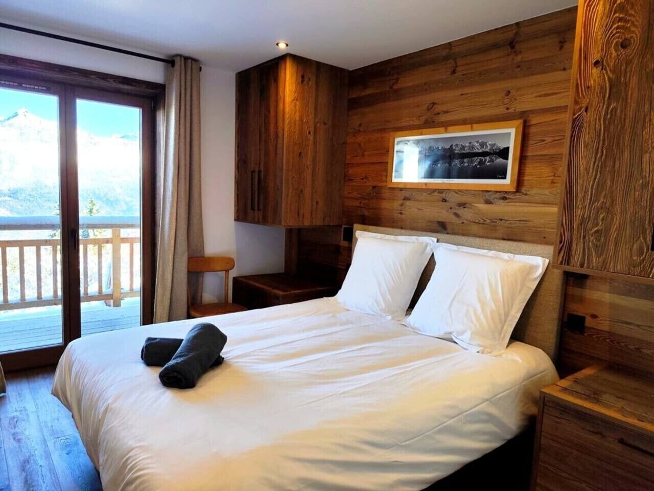 Ein Schlafzimmer mit einem hölzernen Kopfteil, einem Bett mit weißen Leinen, einem Nachttisch und einem Fenster mit Bergblick.