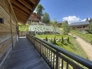 Ein Holzhaus mit Balkon, das einen angelegten Bereich mit Steinmauer und Holzzaun überblickt.