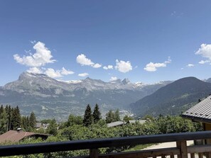 Eine Berglandschaft mit blauem Himmel, einer Holzterrasse und Gebäuden im Vordergrund.