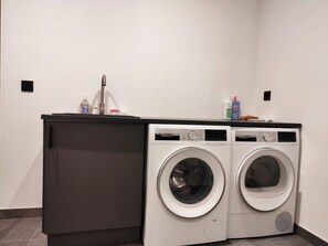 Zona de bugaderia amb dues rentadores de càrrega frontal i un armari de fusta fosca.