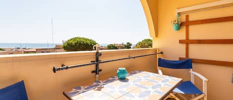 A balcony with a table and chairs, a view of the sea, and a hanging basket with utensils.