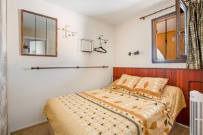 Ein Schlafzimmer mit Bett, Spiegel, Pendelleuchte und einem Fenster mit Vorhängen.