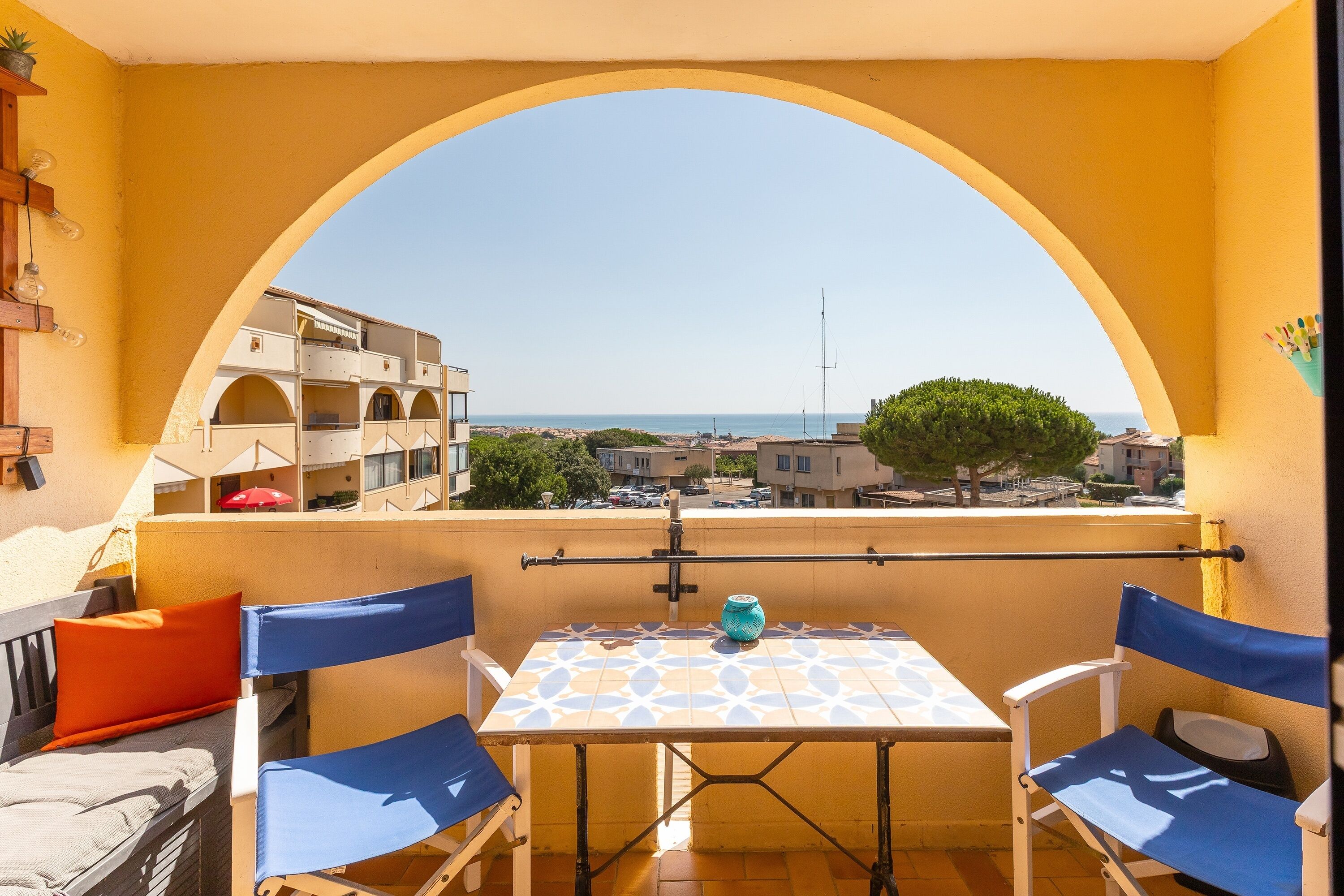 A balcony with a table and chairs, a view of the sea, and a building in the background.