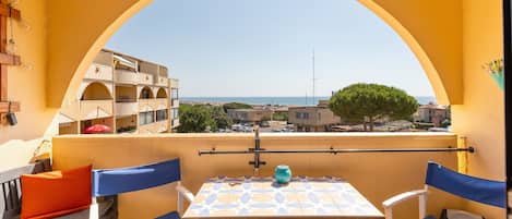 A balcony with a table and chairs, a view of the sea, and a building in the background.