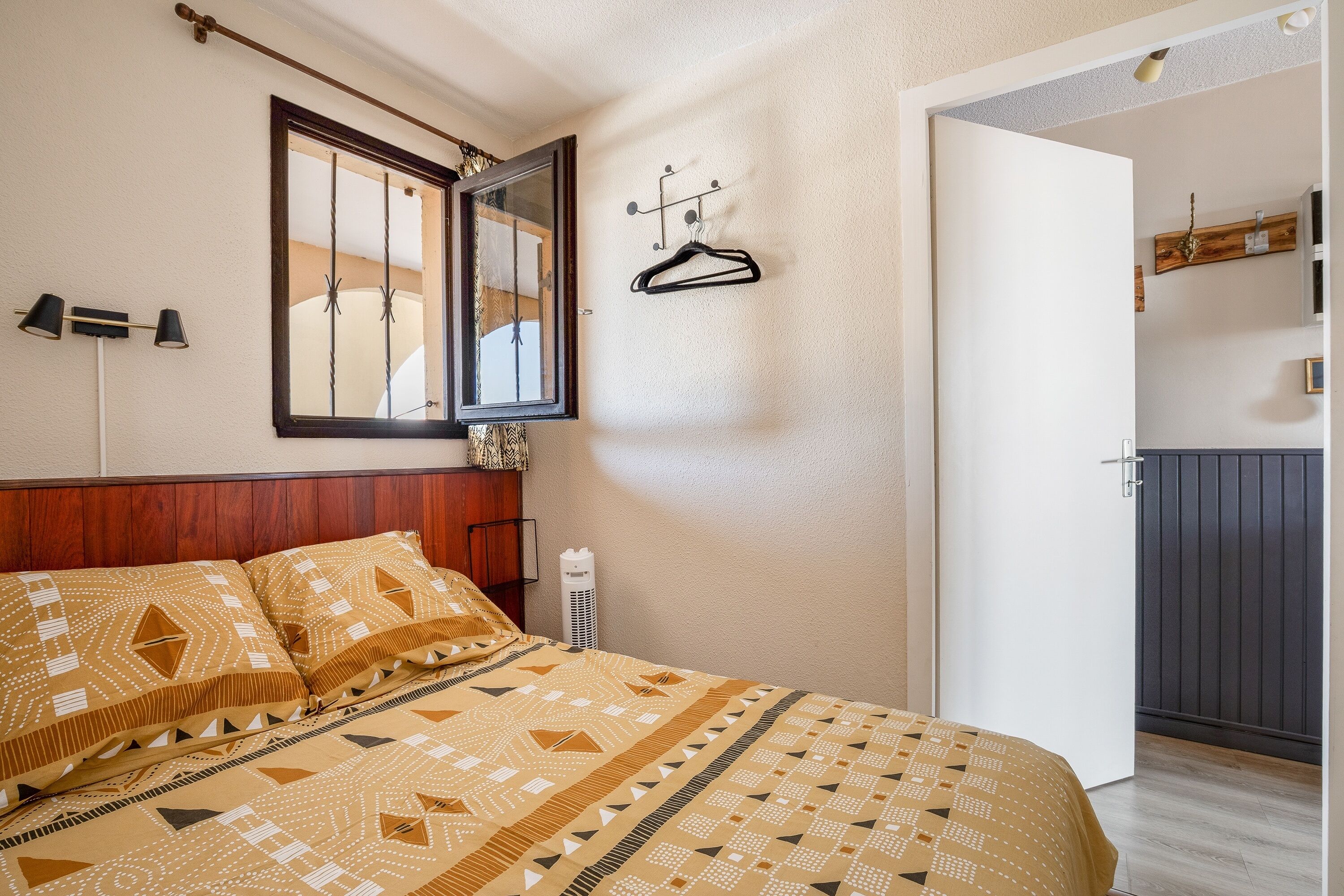 Een slaapkamer met een bed, een spiegel, een hanglamp en een deur naar een andere kamer.