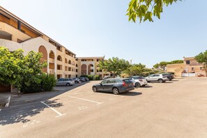 A parking lot with multiple cars, a building with arched windows, and a clear sky. - Chez MarieDo - Bel appt pour 2 avec balcon vue mer (Fleury)