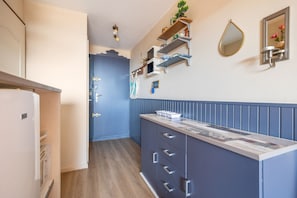 A kitchen with a built-in island, a refrigerator, and a blue accent wall. - Chez MarieDo - Bel appt pour 2 avec balcon vue mer (Fleury)