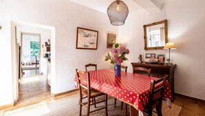 En matplats med ett rött bordslinne med vita prickar, trästolar, en vas med blommor, en hängande lampa och en spegel på väggen.