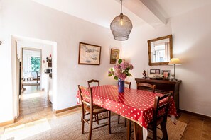 Ein Essbereich mit rotem Tisch, der mit einem Tischläufer mit weißen Punkten bedeckt ist, Holzstühle, einer Blumenvase, einer Hängelampe und einem Spiegel an der Wand.