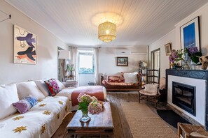 Een knusse woonkamer met een open haard, een zithoek, een bijzettafeltje met een bloevas en een boekenkast.