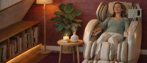 A massage chair in a room with a bookshelf, a small table with a candle, and a potted plant.