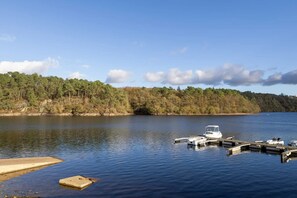 A calm lake with a dock and boats, surrounded by a forested shoreline. - Guest Room "Chambre Cosy à l’écrin de bois" with Terrace, Shared Garden, and Wi-Fi (Guerlédan)