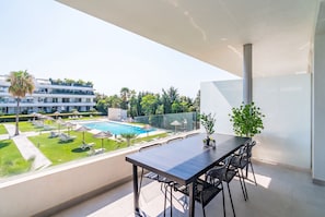 A balcony with a table and chairs, overlooking a swimming pool and a landscaped garden. - Cubo's Bel-Air Estepona Apartment / communal pool / parking included / air conditioning / free Wi-Fi (Estepona)
