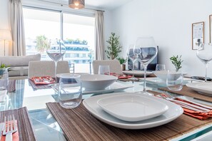 A modern dining area with a glass table, white plates, and clear glassware. - Cubo's Bel-Air Estepona Apartment / communal pool / parking included / air conditioning / free Wi-Fi (Estepona)